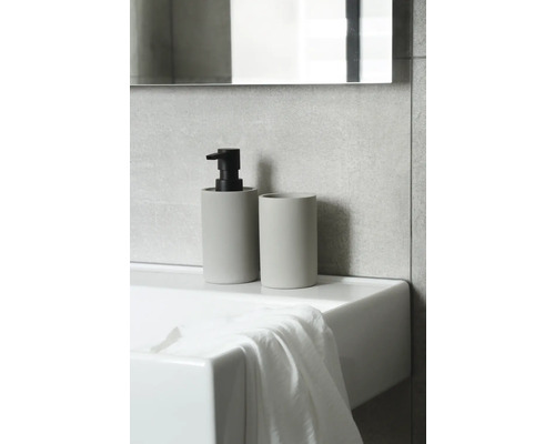 Dávkovač mýdla a kelímek na zubní kartáčky na umyvadle v koupelně.