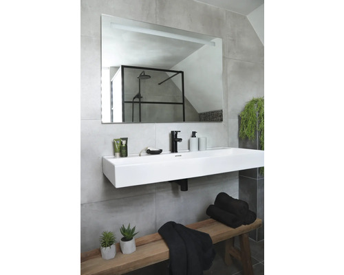 Moderní koupelna s obdélníkovým zrcadlem, umyvadlem na desku, baterií, ručníky a dřevěnou lavicí.