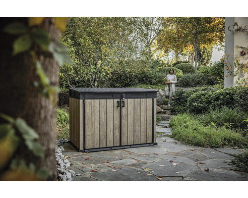 Zahradní skříň na nářadí s dřevěným efektem a žena v pozadí v zahradní krajině