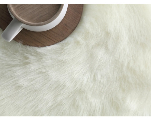 Detailní pohled na koberec s dlouhými vlákny vedle šálku na dřevěném podšálku.