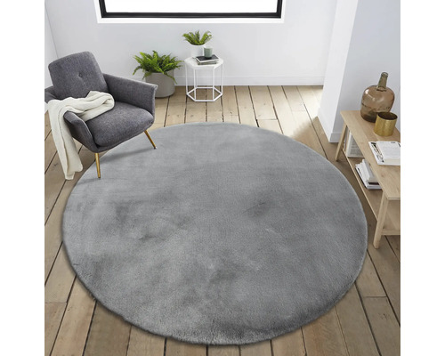 Interiérová scéna s kulatým šedým kobercem, křeslem a odkládacím stolkem