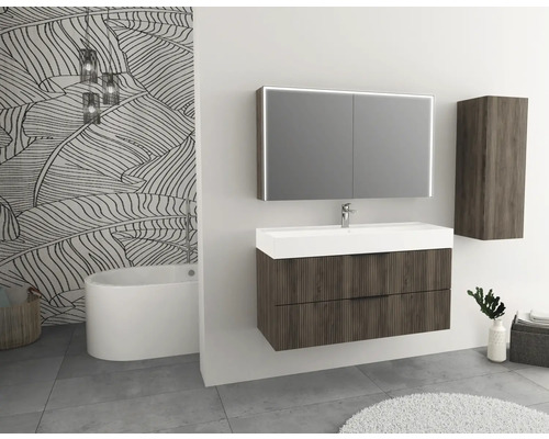 Koupelna s umyvadlem, zrcadlovou skříňkou a vysokou skříňkou ve vzhledu dřeva a vanou před stěnou se vzorem