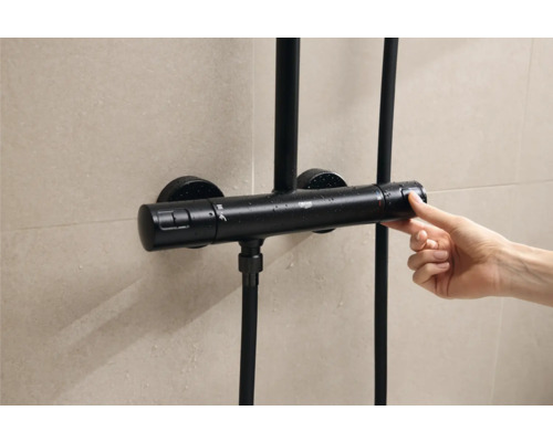 Černý sprchový termostat ovládaný rukou před obloženou stěnou