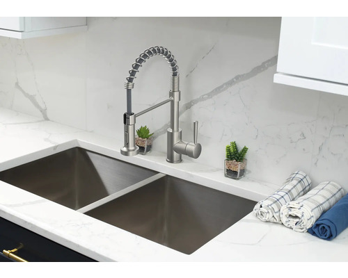 Nerezový kuchyňský dřez s baterií a utěrkami na mramorové desce.