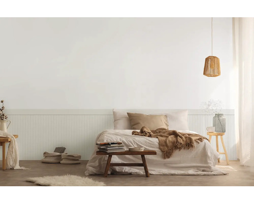 Ložnice s postelí, nočním stolkem, lampou a dekoracemi ve světlém provedení.