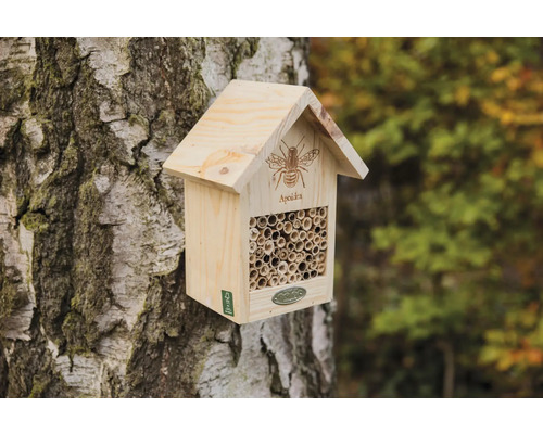 Dřevěný hmyzí hotel na kmeni stromu s trubkami jako hnízdiště