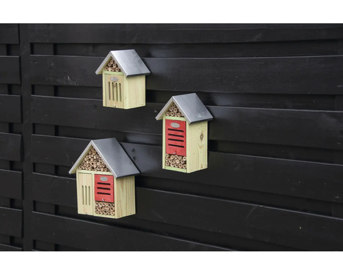 Tři dřevěné hotely pro hmyz s kovovou střechou na plotě