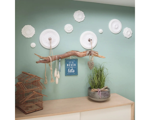 Dekorativní nástěnná dekorace s ozdobnými lištami, věšákem na větve a doplňky na komodě.