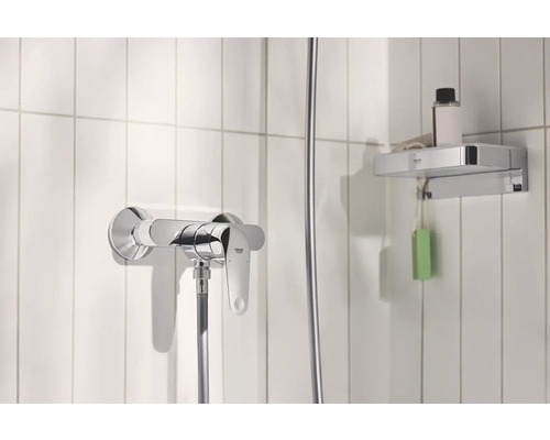 Sprchová baterie a odkládací police v koupelně s bílými obklady.