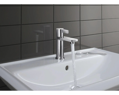 Kovová umyvadlová baterie s proudem vody na bílém umyvadle