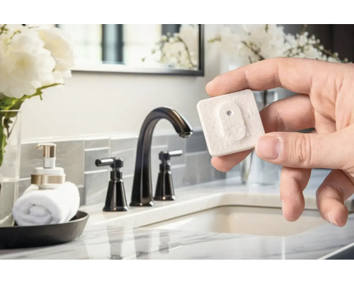 Ruka drží detektor vody v koupelně s umyvadlem a baterií