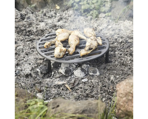 Kulatý grilovací rošt s kuřecími paličkami stojí nad táborákem.