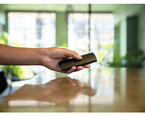 Ruka drží černé dálkové ovládání.