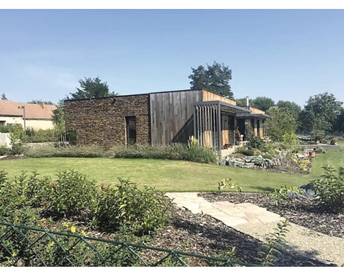 Exteriér moderního domu s kamennou fasádou a dřevěným obkladem, obklopeného udržovanou zahradou.