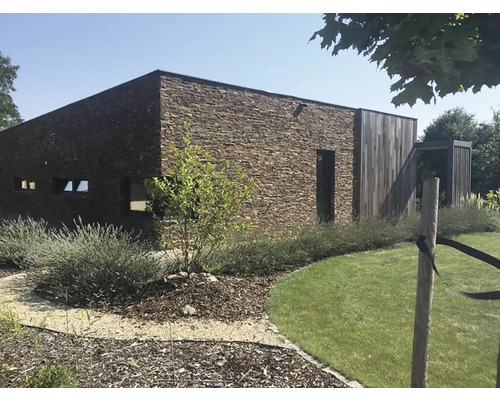 Moderní dům s kamennou zdí a dřevěnými prvky v zahradě.