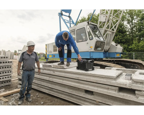 Dva stavební dělníci se staveništním rádiem a prefabrikovanými betonovými díly před jeřábem