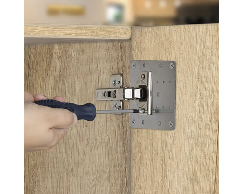 Osoba připevňuje šroubovákem desku pantu nábytkových dveří na dřevěné dveře.