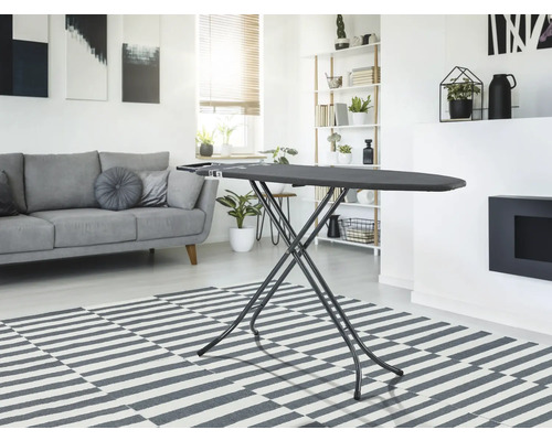 Žehlicí prkno v obývacím pokoji se světlou pohovkou a kobercem.