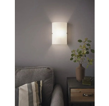 Skleněná nástěnná lampa vedle pohovky a nočního stolku v obývacím pokoji.