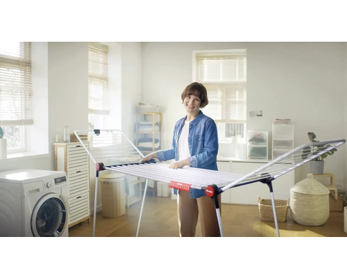 Žena ve světlé místnosti vedle sušáku na prádlo a pračky.