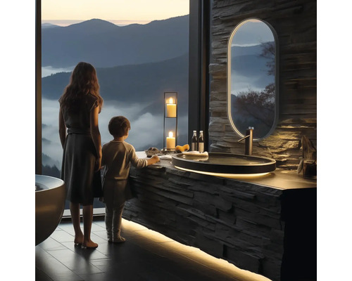 Světlá koupelna s kamenným umyvadlem, zrcadlem a výhledem na hory. U umyvadla stojí žena a dítě.