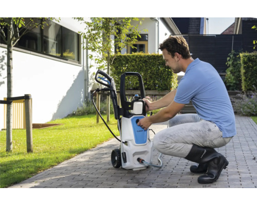 Muž obsluhuje vysokotlaký čistič na zahradě.