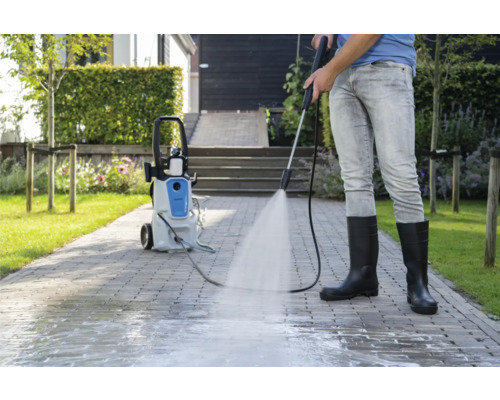 Osoba čistí dlažební kostky vysokotlakým čističem venku.