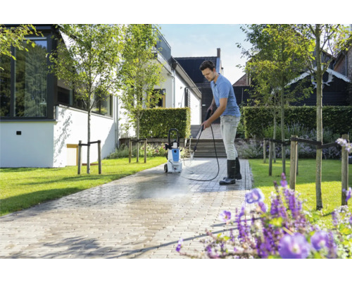 Muž čistí dlažební kostky vysokotlakým čističem před domem.