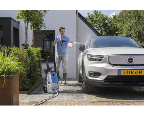 Muž čistí auto vysokotlakým čističem venku.