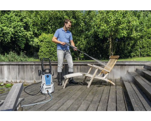 Muž čistí dřevěnou židli vysokotlakým čističem venku.