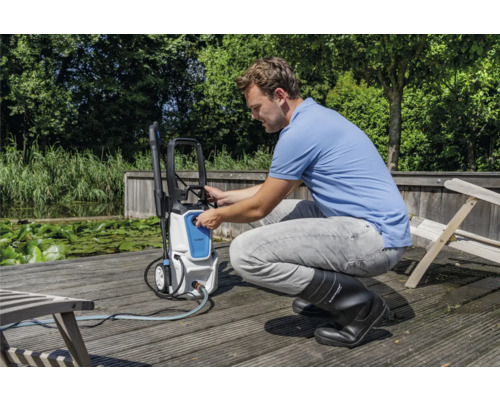 Muž obsluhuje vysokotlaký čistič venku na dřevěné terase u vodní plochy