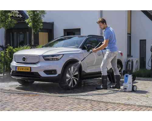 Muž čistí auto vysokotlakým čističem před domem