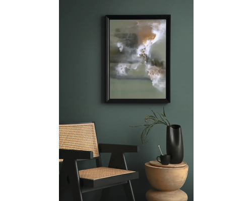 Scéna s abstraktním uměleckým dílem v rámu, ratanovým křeslem a odkládacím stolkem s dekorací.