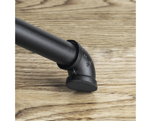 Detailní záběr černé nohy nábytku v industriálním designu s trubkovými prvky na dřevěné podlaze.
