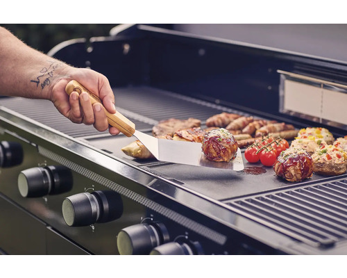 Plynový gril s grilovaným jídlem a grilovacím náčiním v provozu