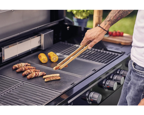 Muž griluje klobásy a kukuřičné klasy na grilu