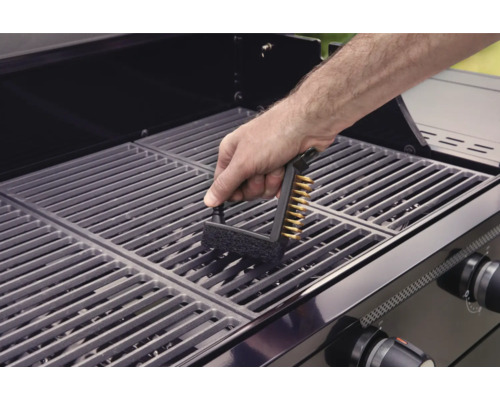 Osoba čistí grilovací rošt grilovacím kartáčem.