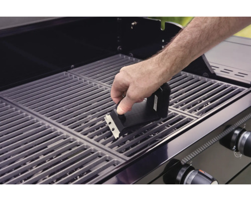 Osoba čistí grilovací rošt grilovacím kartáčem.