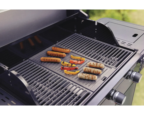 Plynový gril s klobásami a paprikami na grilovací mřížce.