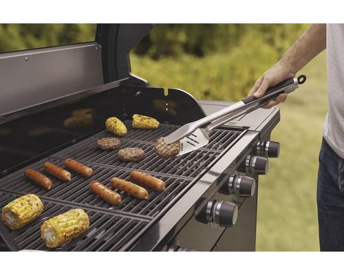 Gril s grilovanými klobásami, hamburgery a kukuřičnými klasy, obsluhovaný grilovacím náčiním