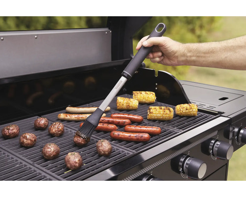 Grilovací scéna s grilovacím kartáčem, klobásami, kukuřičnými klasy a masovými kuličkami na plynovém grilu.