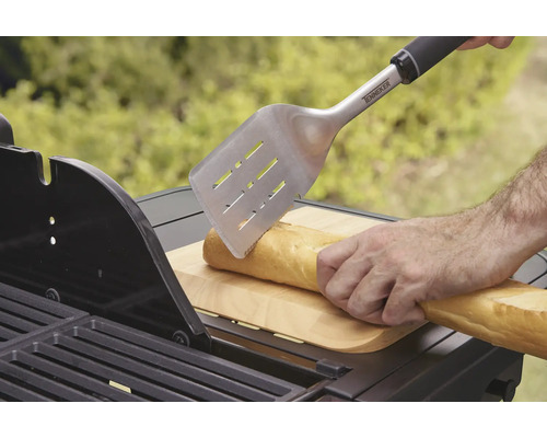 Osoba krájí bagetu grilovací obracečkou na grilu.