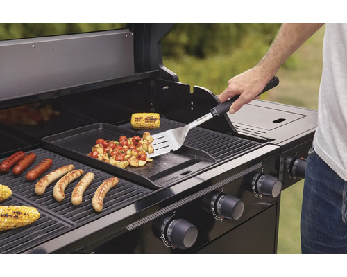 Osoba griluje klobásy, kukuřici a zeleninu na plynovém grilu.