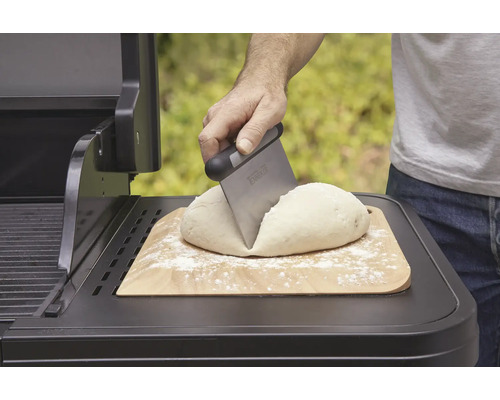 Těsto na dřevěné desce se dělí škrabkou na těsto na grilu