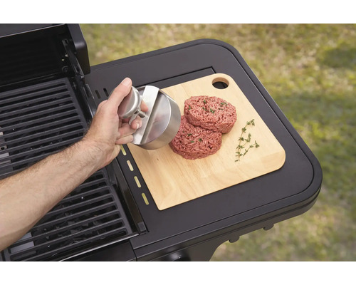 Osoba formuje pomocí lisu na hamburgery maso na hamburgery na prkénku vedle grilu.