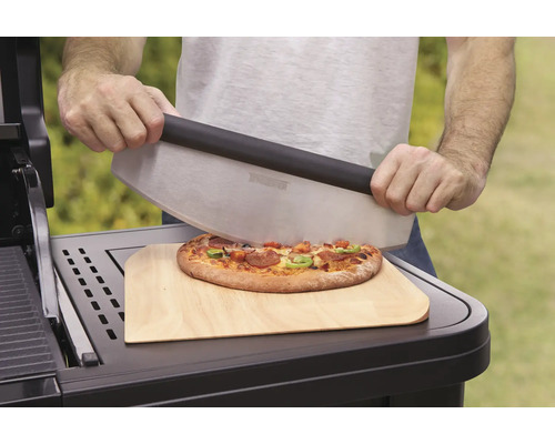 Osoba krájí pizzu kráječem na pizzu na dřevěném prkénku.