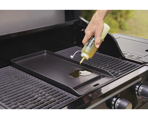 Osoba nalévá olej na grilovací desku na plynovém grilu.
