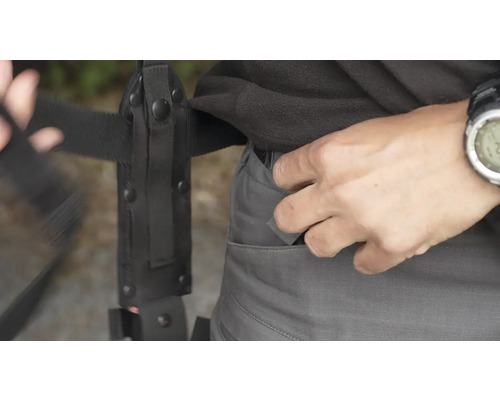 Osoba ukládá nůž do kapsy kalhot vedle pouzdra na nůž na opasku