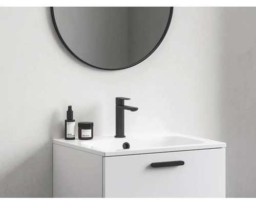 Pohled na koupelnu s kulatým zrcadlem, skříňkou pod umyvadlo, baterií a pečujícími produkty