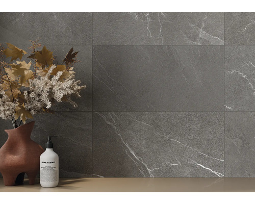 Šedé dlaždice s mramorovým vzhledem na stěně, doplněné vázou s květinovou výzdobou a lahvičkou mýdla